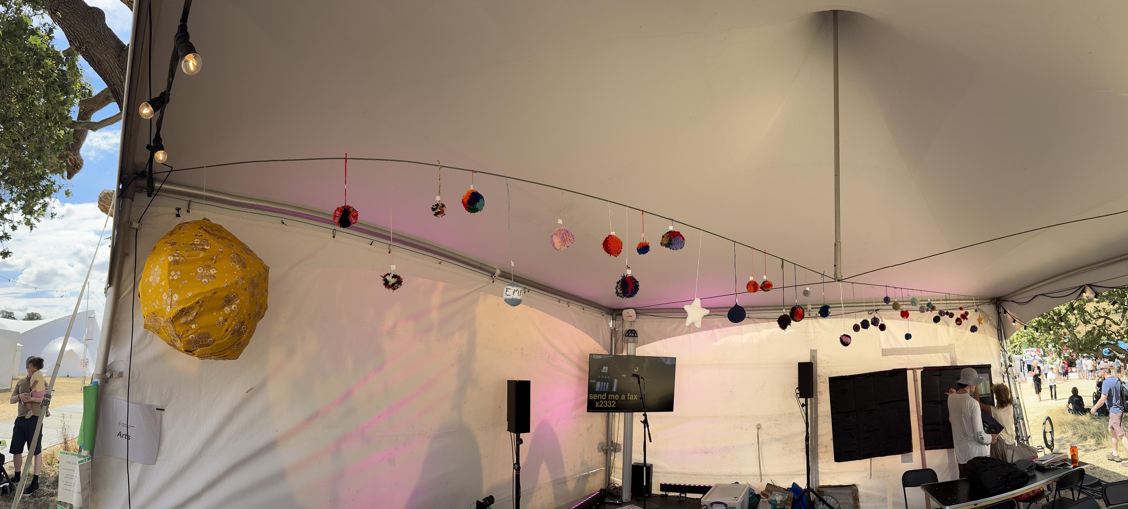 Multiple fabric craft planets made individually by workshop participants hanging from a string inside the arts tent at EMF. On the left is a larger body representing the sun.